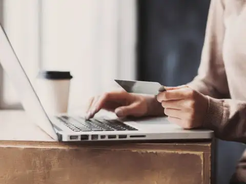 Person making an online purchase with credit card while drinking coffee